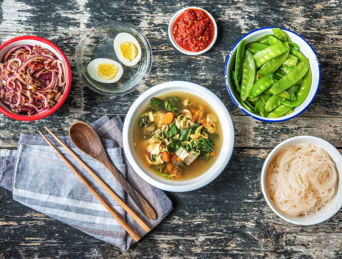 Indonesische soto met een gekookt ei, peultjes en rijstvermicelli