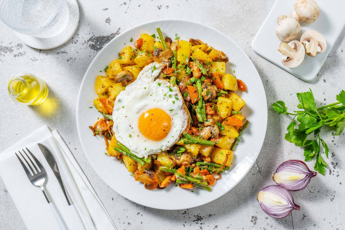 Pommes de terre et légumes sautées garnis de fromage fondu et œuf au plat