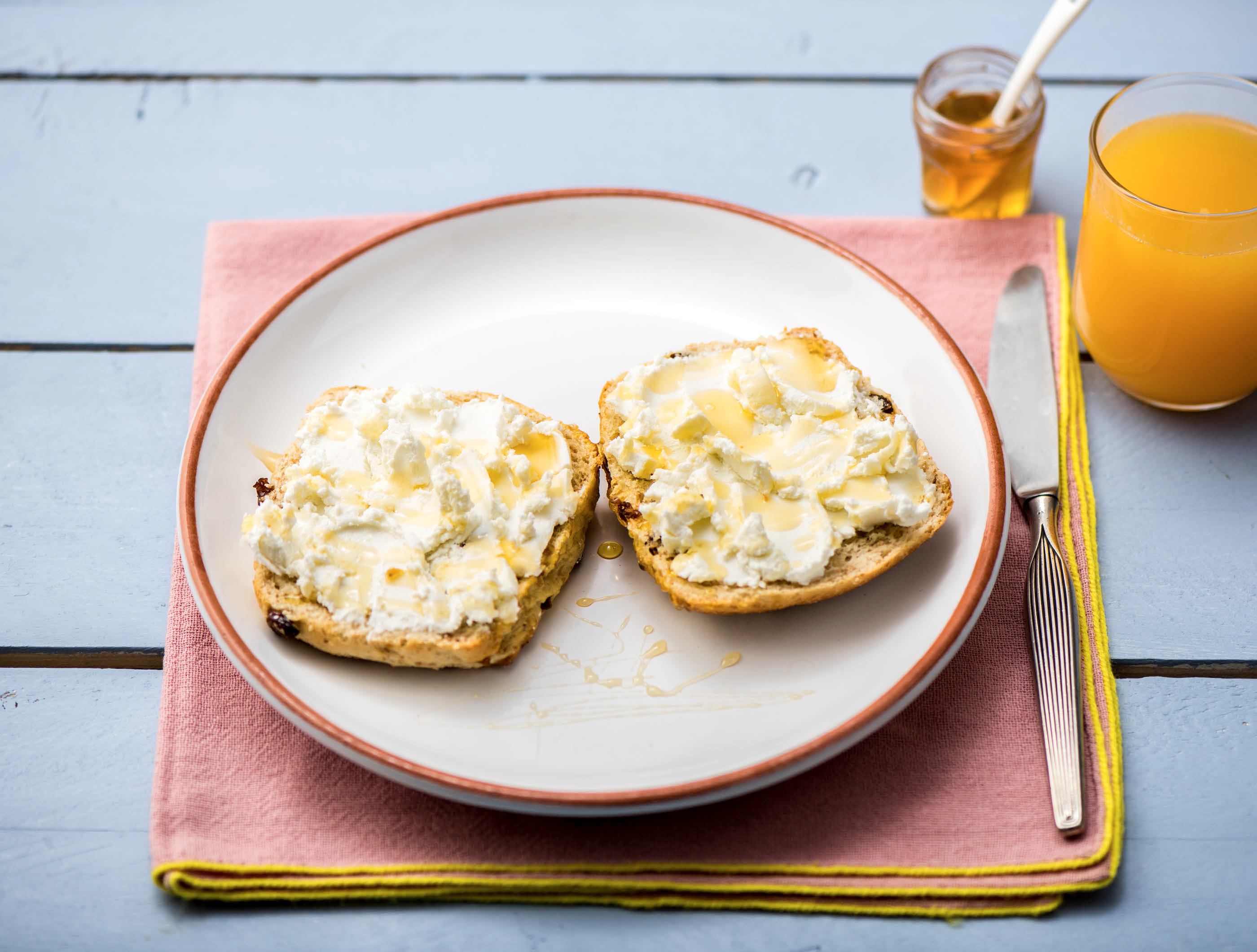 Volkoren rozijnen-notenbroodje met geitenkaas, honing en vers sinaasappelsap