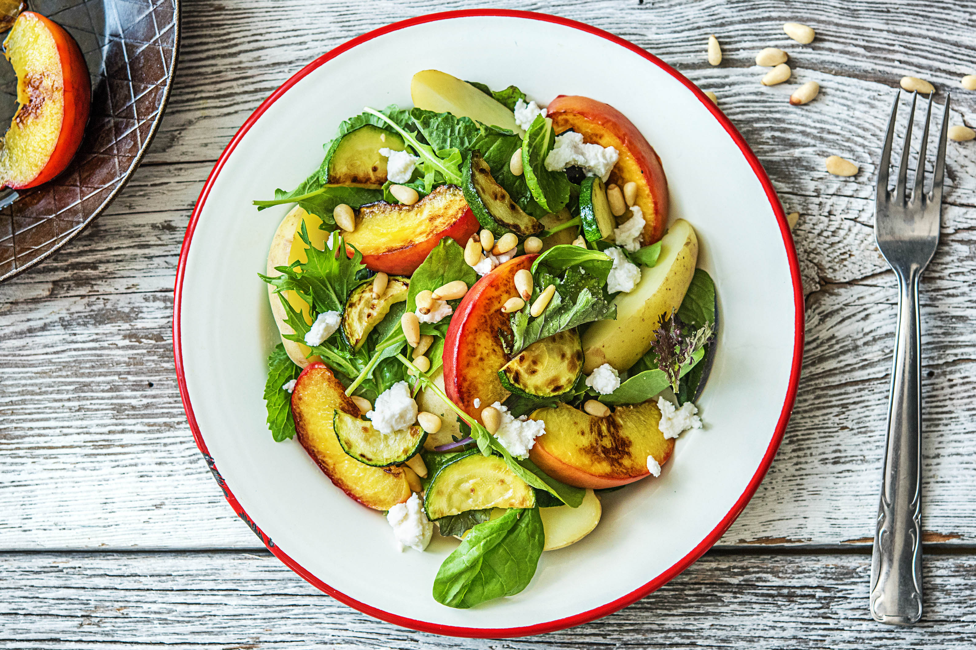 Lauwwarme salade met gebakken perzik, geitenkaas, krieltjes, courgette en pijnboompitten