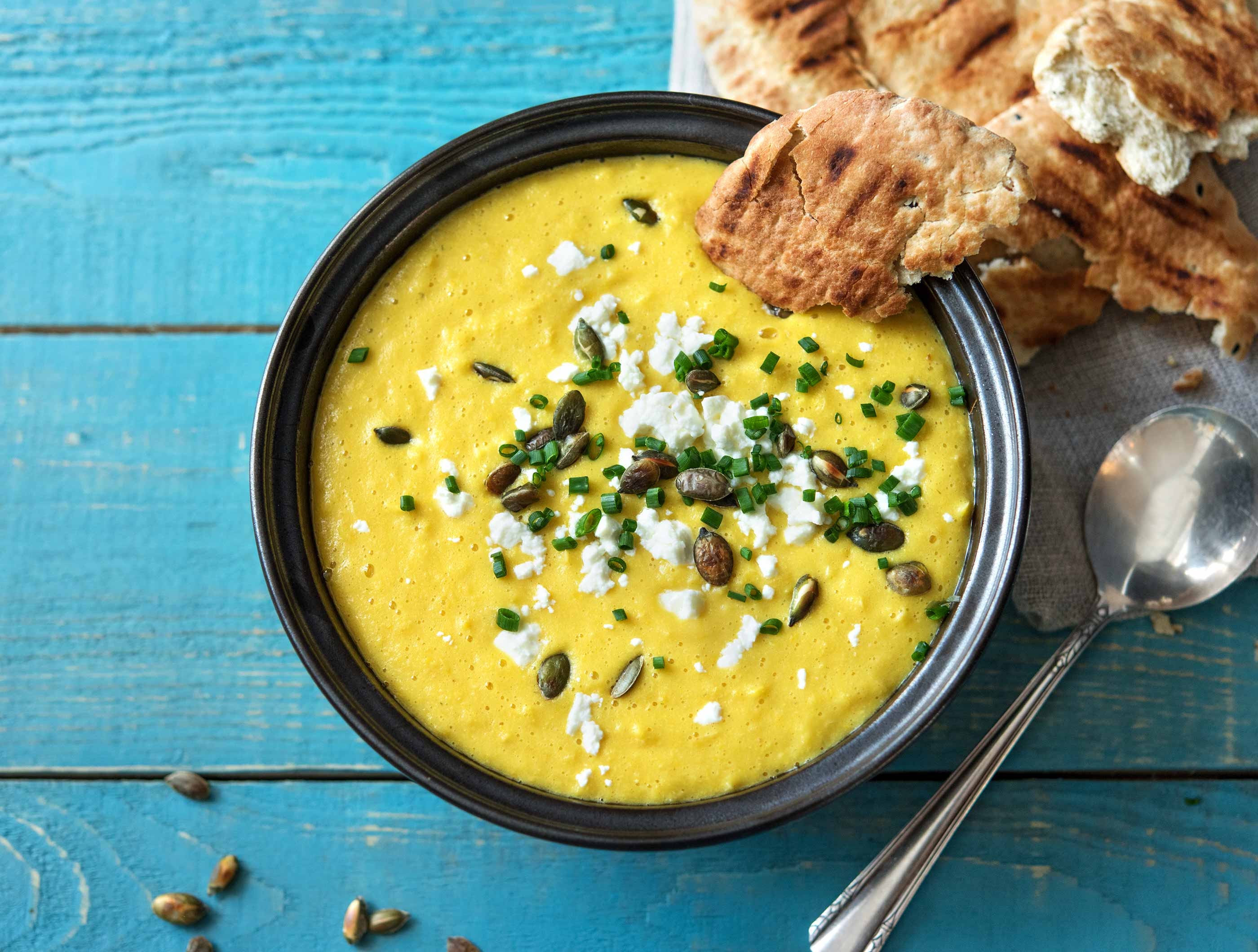 Soupe au poivron jaune et au maïs avec feta, graines de courge, pain naan