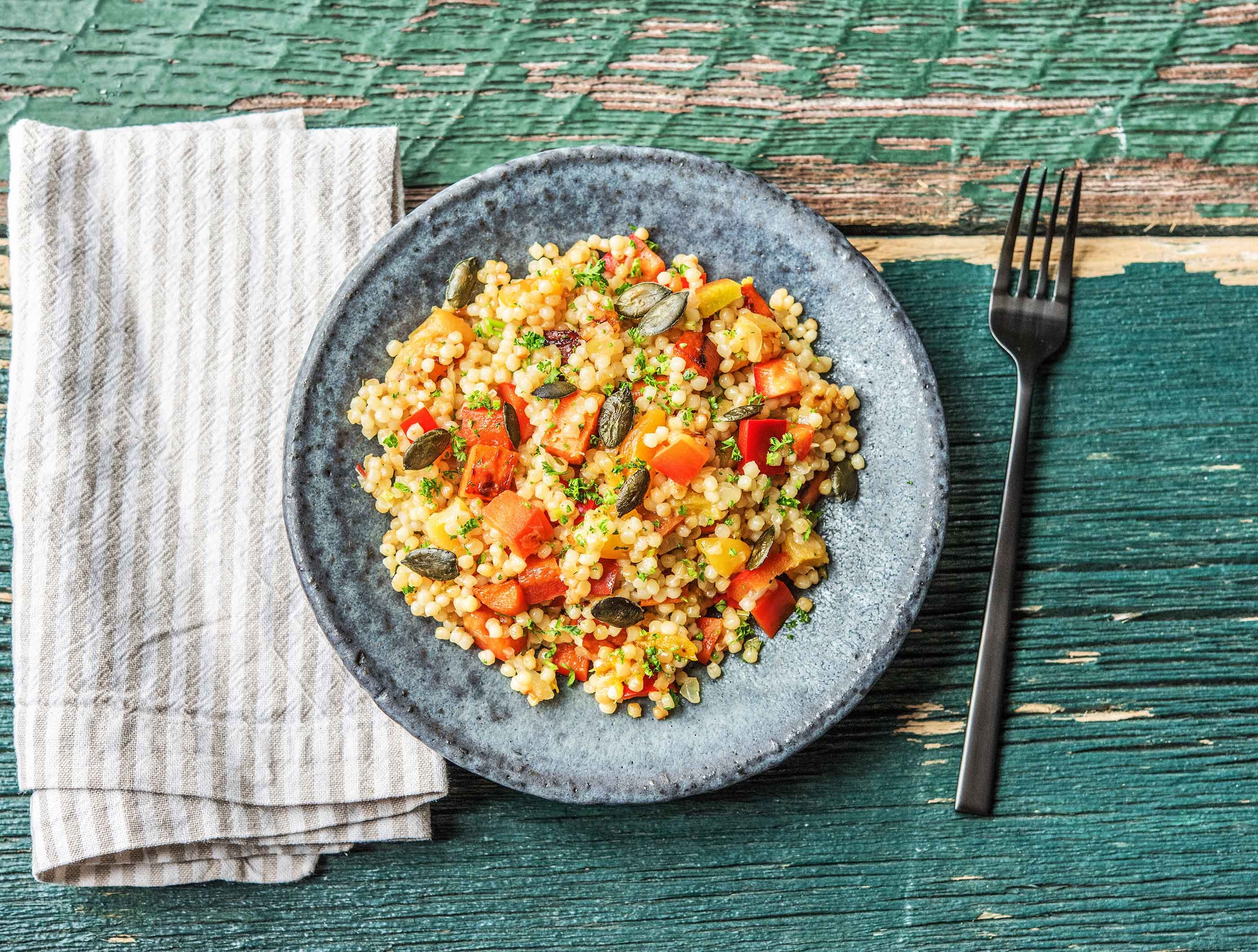 Rode parelcouscous met puntpaprika, abrikozen, pompoenpitten, peen en krulpeterselie