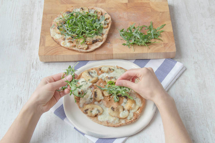 Top pizzas with fresh rocket and a bit of olive oil