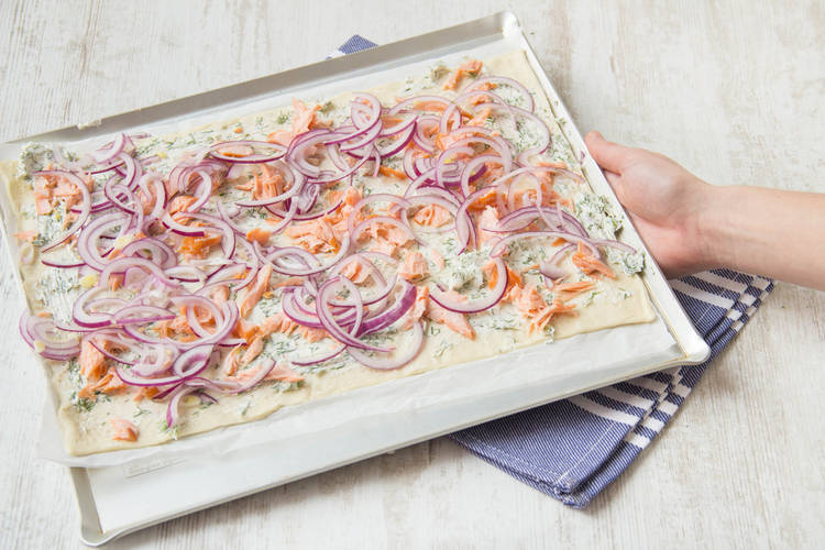 Den Pizzateig belegen