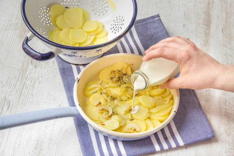 Die Kartoffeln und die Zutaten des Gratins in einer Auflaufform vermengen