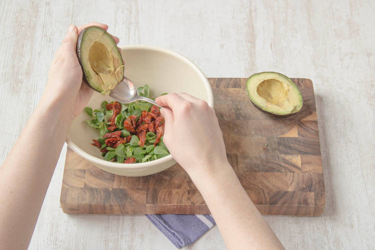Meng de veldsla, semi-zongedroogde tomaten, avocado en tijm in een saladekom.