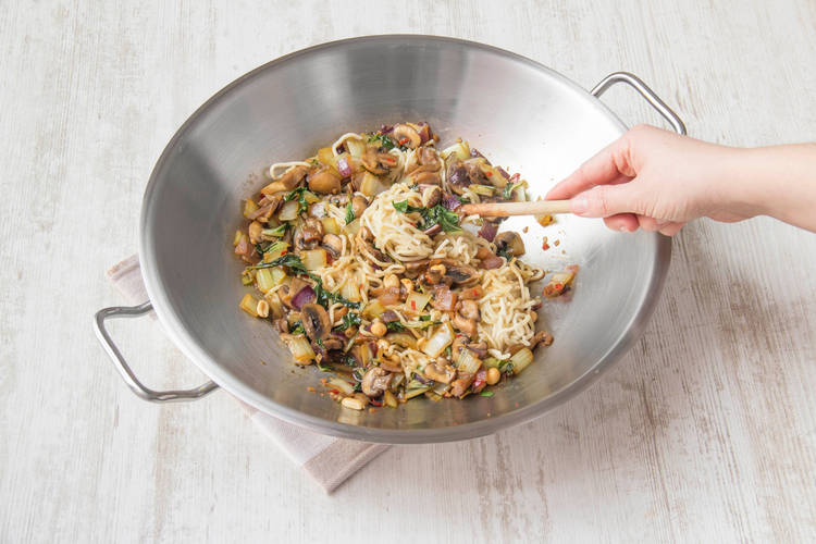 Voeg de noedels en de helft van de pinda’s toe aan de wok