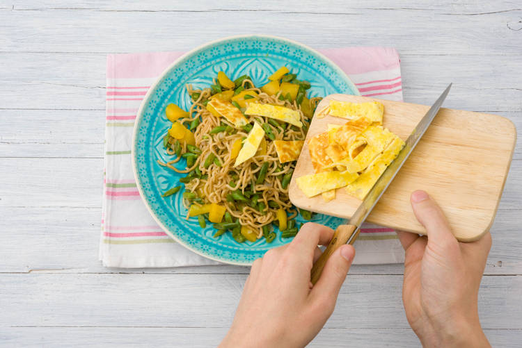 Serveer de bami met de omeletreepjes en de pinda's