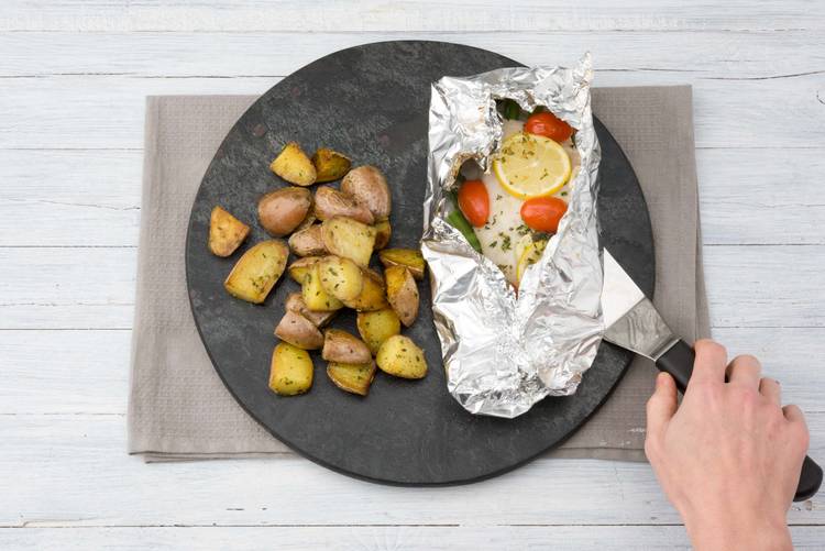 Verdeel de aardappelen en vispakketjes over de borden.