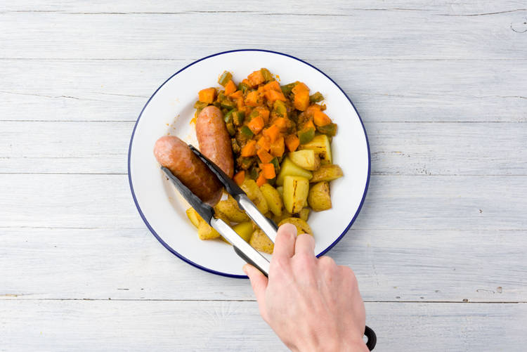 Verdeel de wildzwijnworstjes, de ratatouille en de krieltjes over de borden.