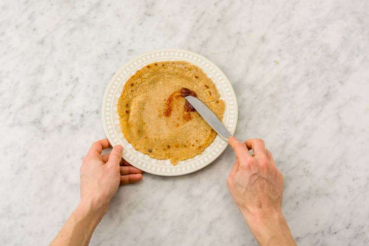 Smeer de pannenkoeken in met de jam en bestrooi met de rozijnen.