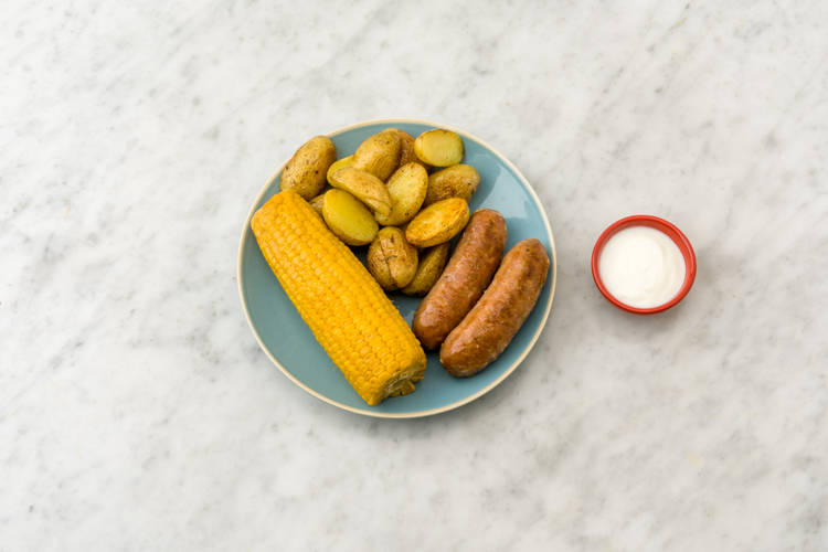 Verdeel de kipsaucijsjes, maïskolf en krieltjes over de borden.