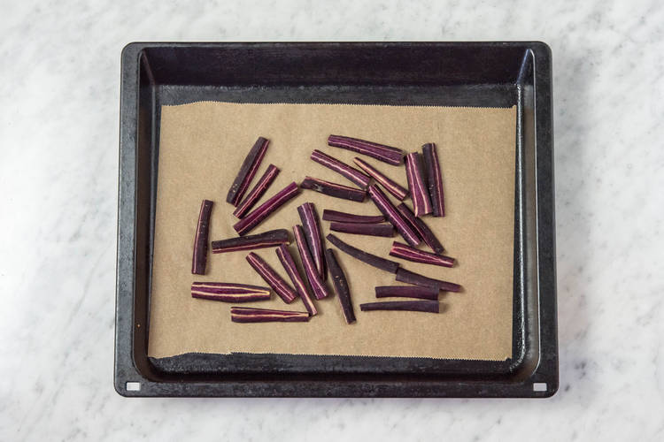 Karottenstifte auf einem mit Backpapier belegten Backblech verteilen