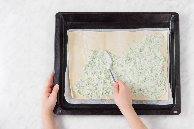 Flammkuchenteig auf ein Backblech ausrollen und mit dem Rucola-Schmand bestreichen