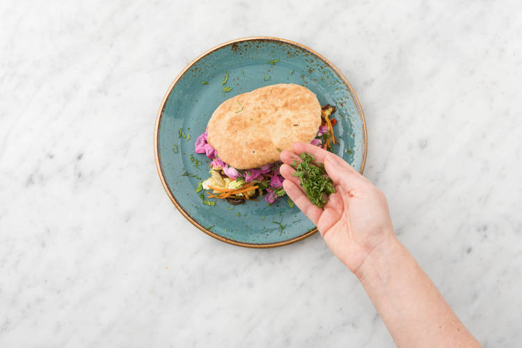 Vul een naanbrood per persoon met achtereenvolgens het groentemengsel, rode bietsalade en yoghurtsaus en bestrooi met de rest van de munt.