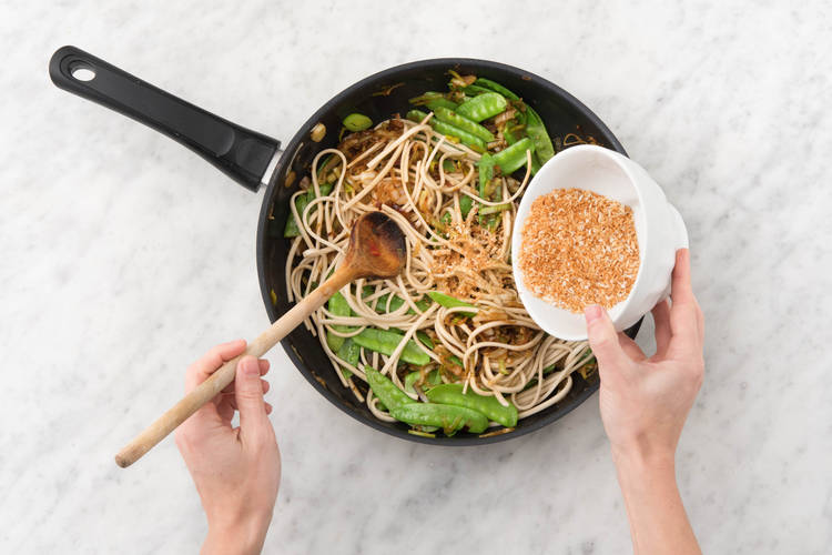 Ajouter les nouilles, la moitié du maquereau fumé et la moitié de la coco râpée au wok