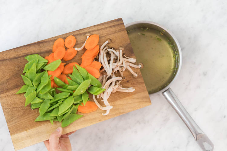 Karottenscheiben, Buchenpilze und Zuckerschoten in die Gemüsebrühe geben