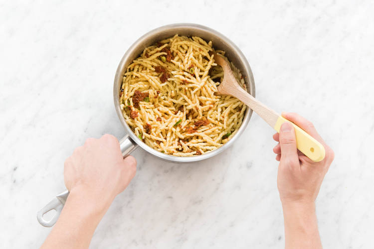 Pasta mit Pesto und Frühlingszwiebeln gut vermischen.