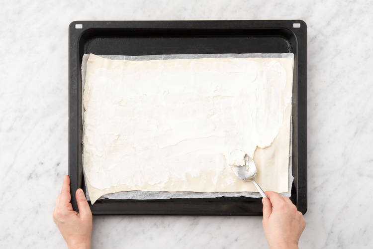 Flammkuchenteig mit Ziegenfrischkäse bestreichen