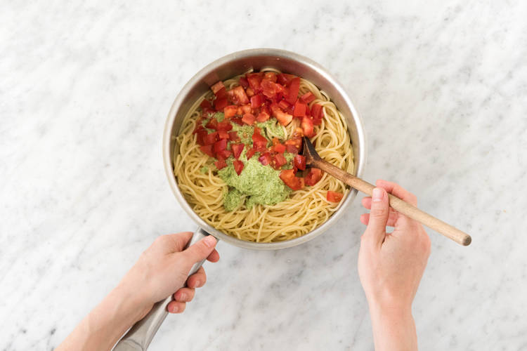 Spaghetti mit Pesto und Tomatenstücken vermischen