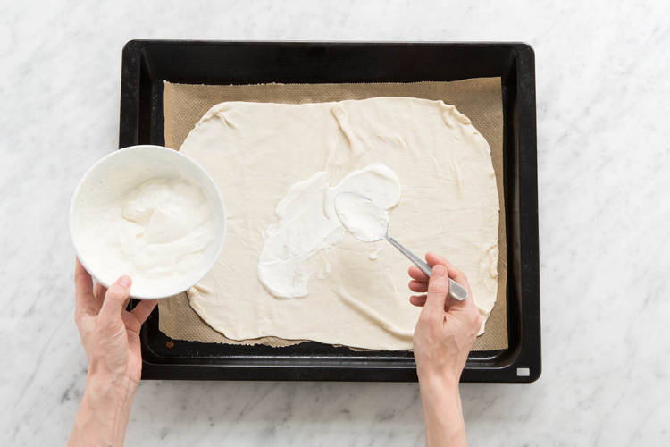 Flammkuchenteig ausrollen und mit dem Schmand bestreichen