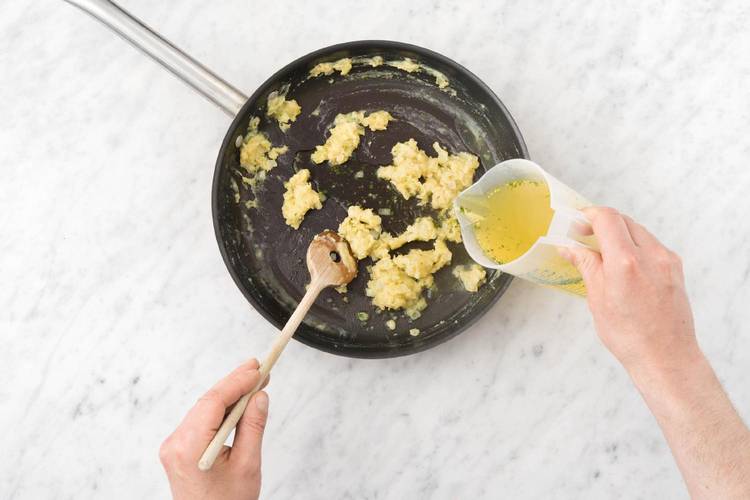 Voeg 1/3 deel van de bouillon toe en roer met een garde tot een glad mengsel